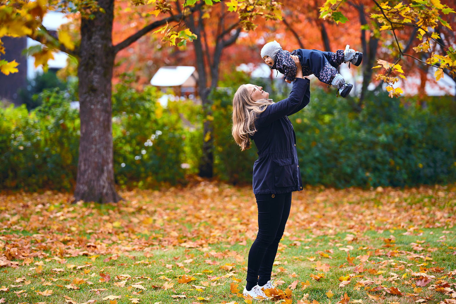Laura Lilleberg nostaa vauvansa ylös käsivarsiensa varaan ja katsoo häntä. Taustalla näkyy kaunista syksyn ruskaa.